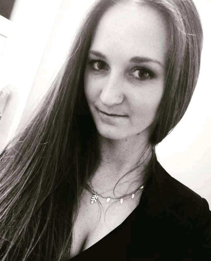 Zdjęcie pani Agaty Karbowskiej. Portret młodej kobiety w czarno-białej tonacji. Ma długie, ciemne włosy i naszyjnik z drobnymi zawieszkami. Patrzy na bok i uśmiecha się.