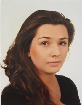 Zdjęcie pani Justyny Warzochy Borawskiej. Portret kobiety z rozpuszczonymi, ciemnymi włosami na neutralnym, jasnym tle. Patrzy prosto przed siebie.